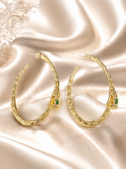 Gold-tone snake hoop earrings with green eye accents on satin background