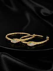 Gold-tone snake hoop earrings with green and crystal-style eye accents on black background