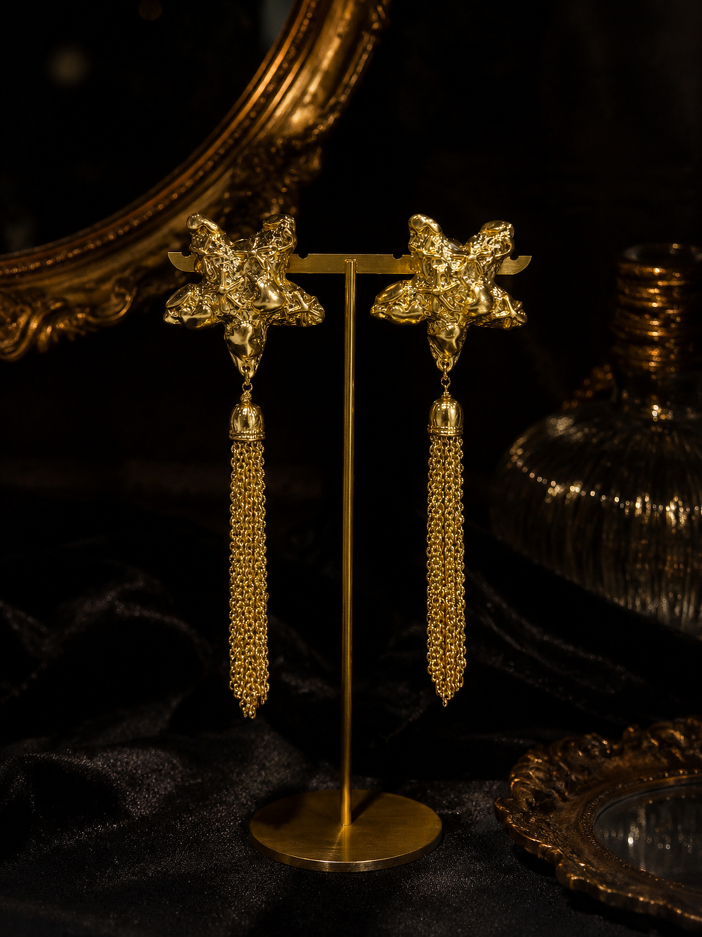 Gold-tone star chain tassel statement earrings front view on a display stand