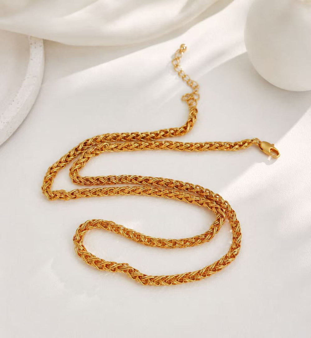 Gold-tone woven chain necklace with lobster clasp on white satin