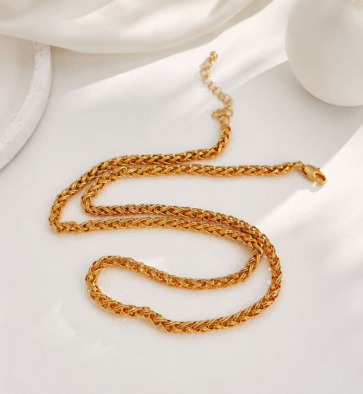 Gold-tone woven chain necklace with lobster clasp on white satin