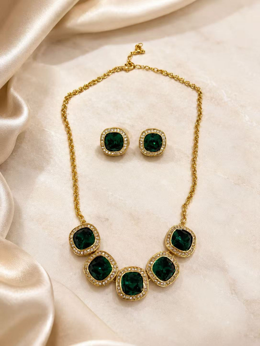 Green rhinestone necklace and matching stud earrings set on champagne fabric