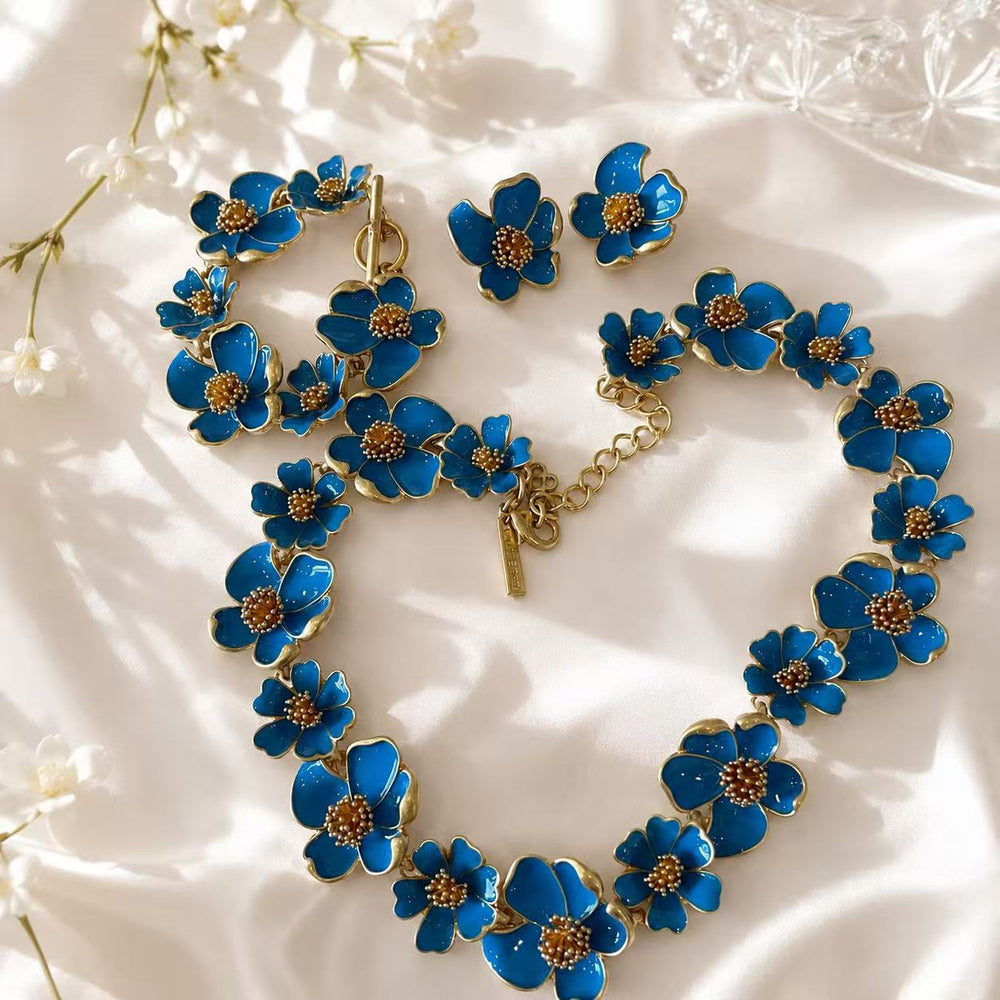 Light blue enamel floral necklace, bracelet, and matching stud earrings complete set on ivory fabric
