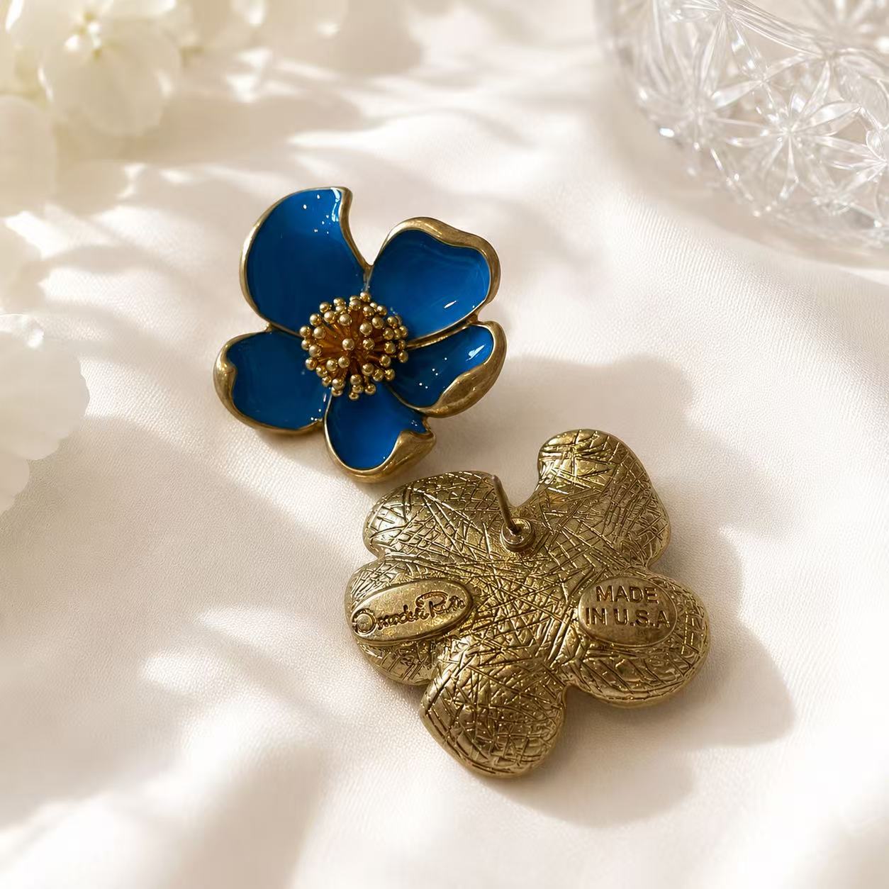 Light blue enamel floral stud earring shown from front and back on ivory fabric