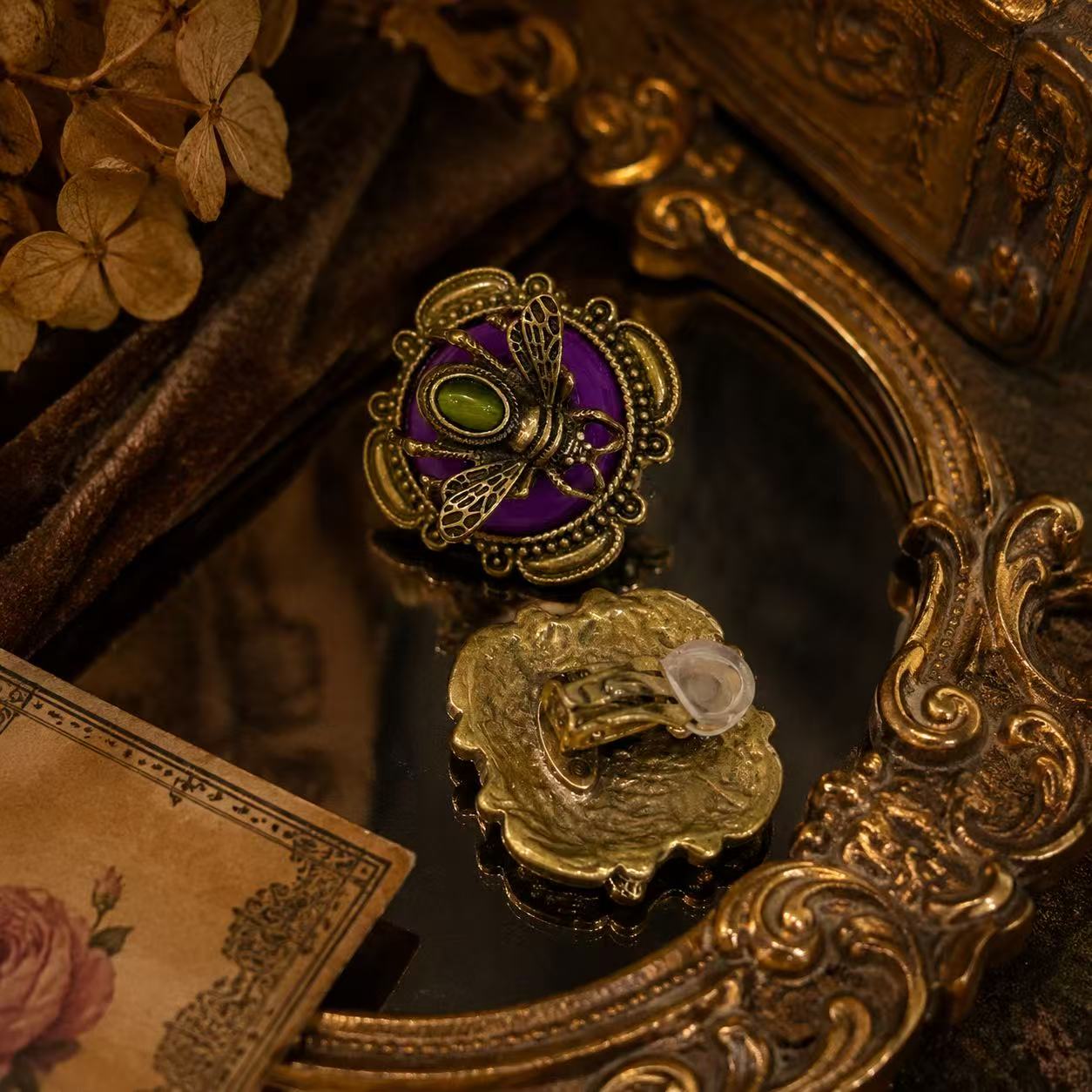 Gold-tone honey bee earring with a purple stone-style background and green cabochon-style center, fastening detail