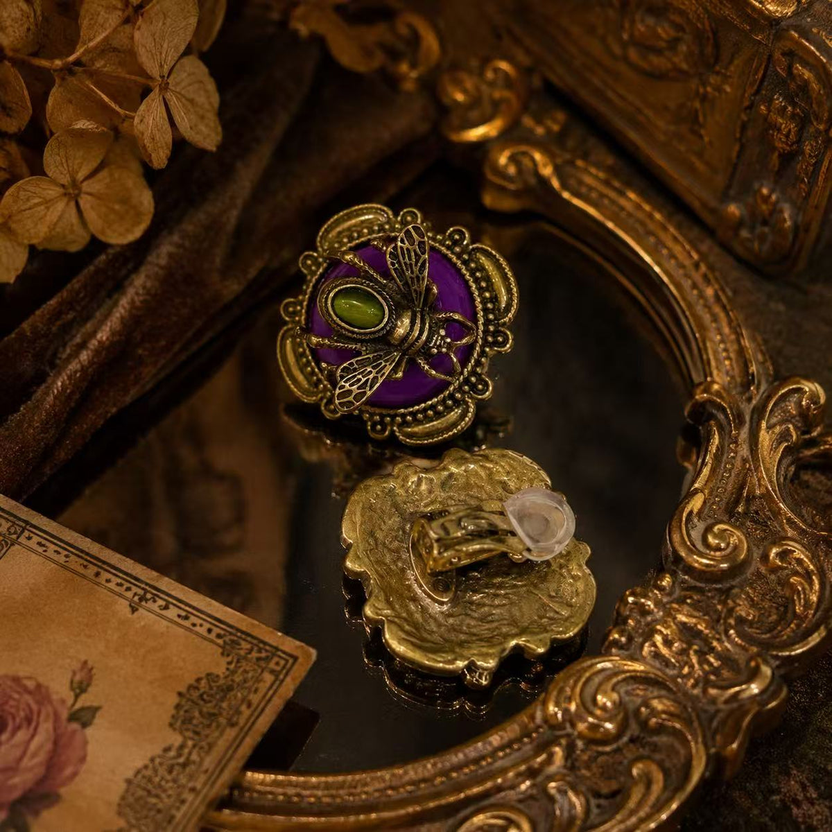 Gold-tone honey bee earring with a purple stone-style background and green cabochon-style center, fastening detail