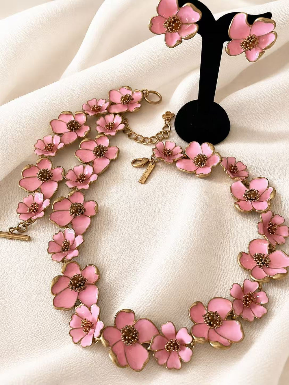 Pink enamel floral necklace, bracelet, and stud earrings complete set on ivory fabric