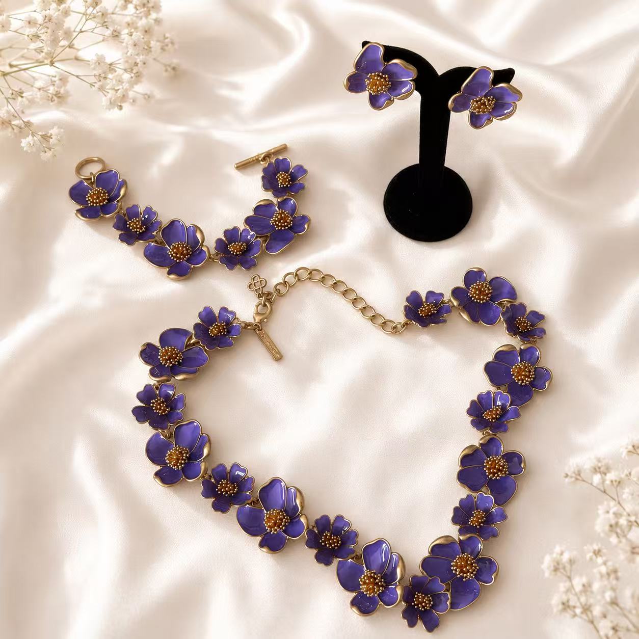 Purple enamel floral necklace, bracelet, and matching stud earrings complete set on ivory satin