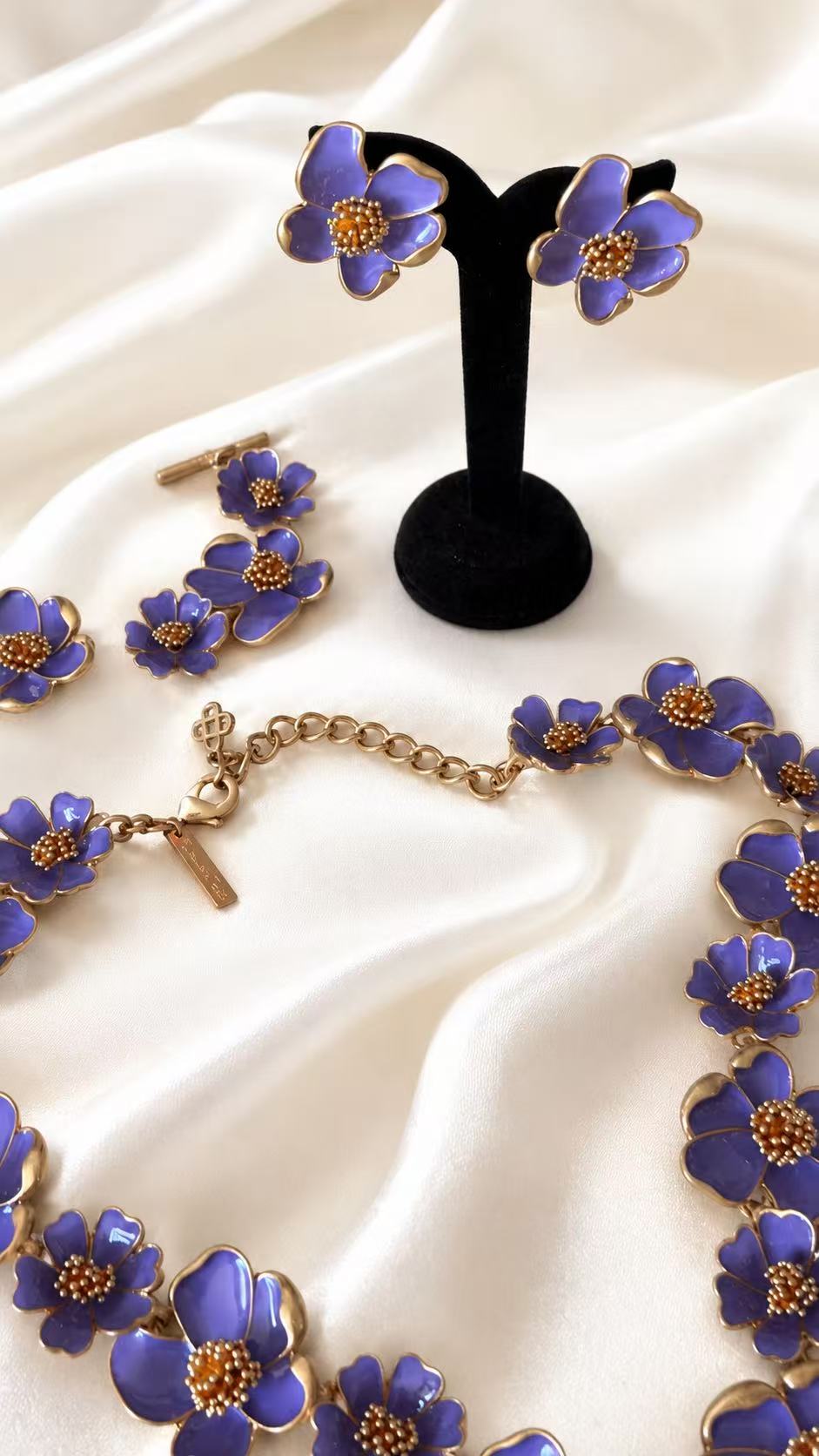 Purple enamel floral necklace, bracelet, and stud earrings detail on ivory satin
