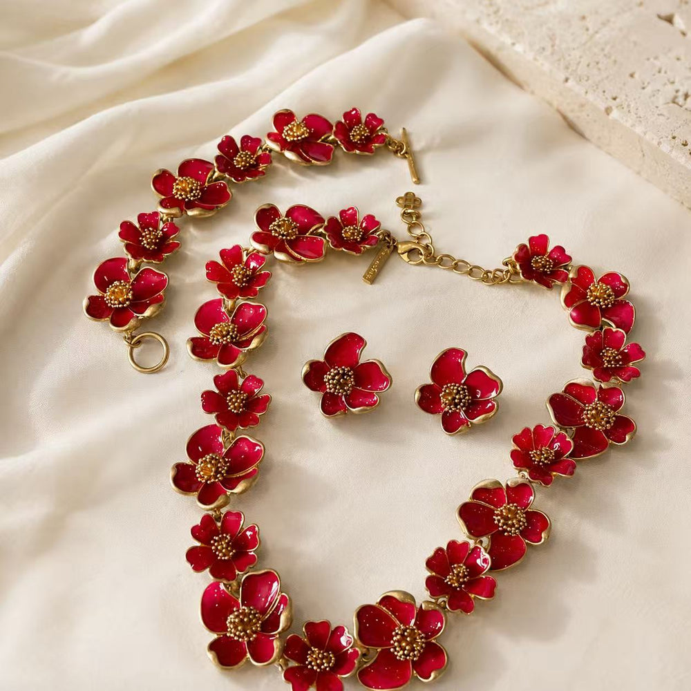 Red enamel floral necklace, bracelet, and matching stud earrings complete set on ivory fabric