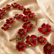 Red enamel floral necklace, bracelet, and stud earrings detail on champagne fabric