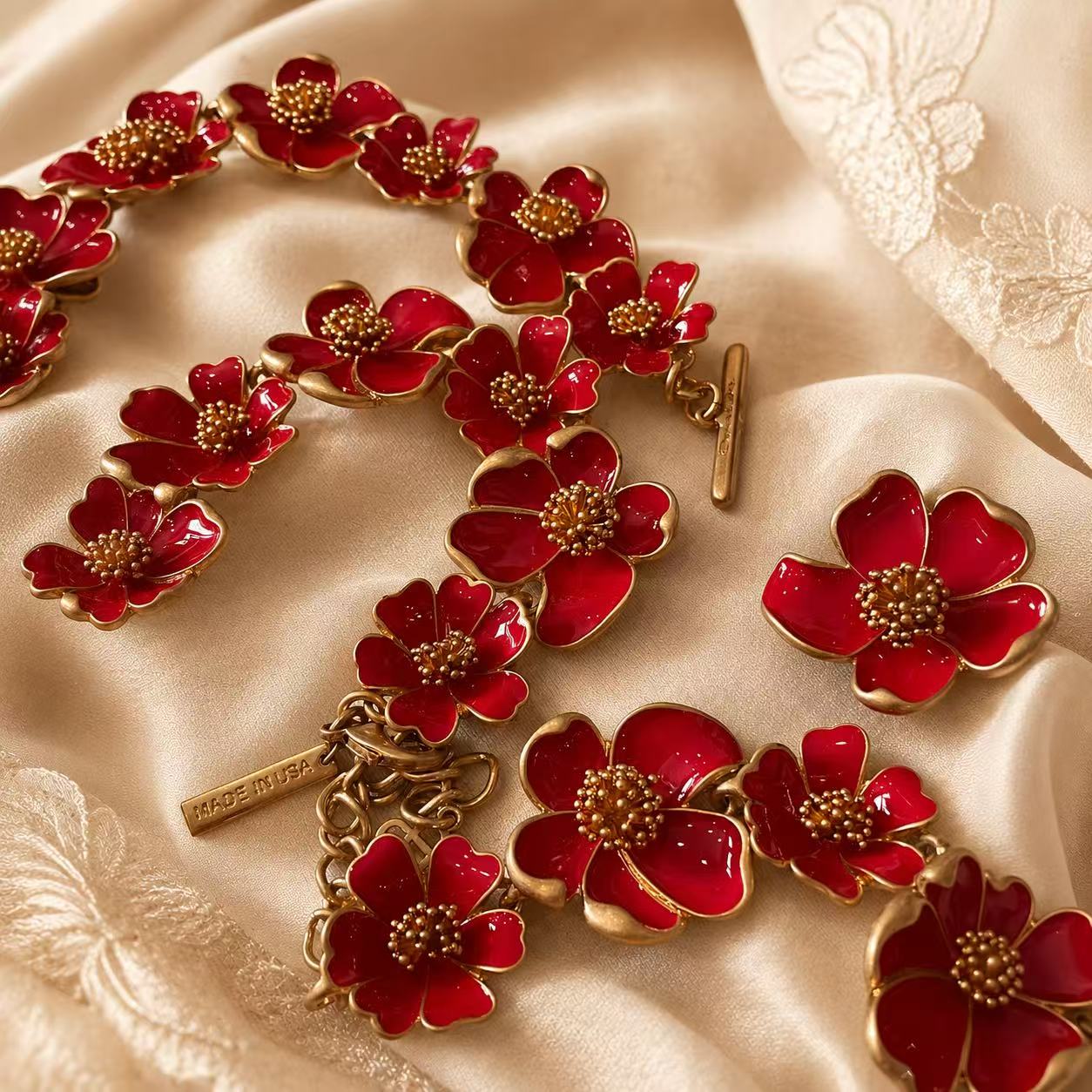 Red enamel floral necklace, bracelet, and stud earrings detail on champagne fabric