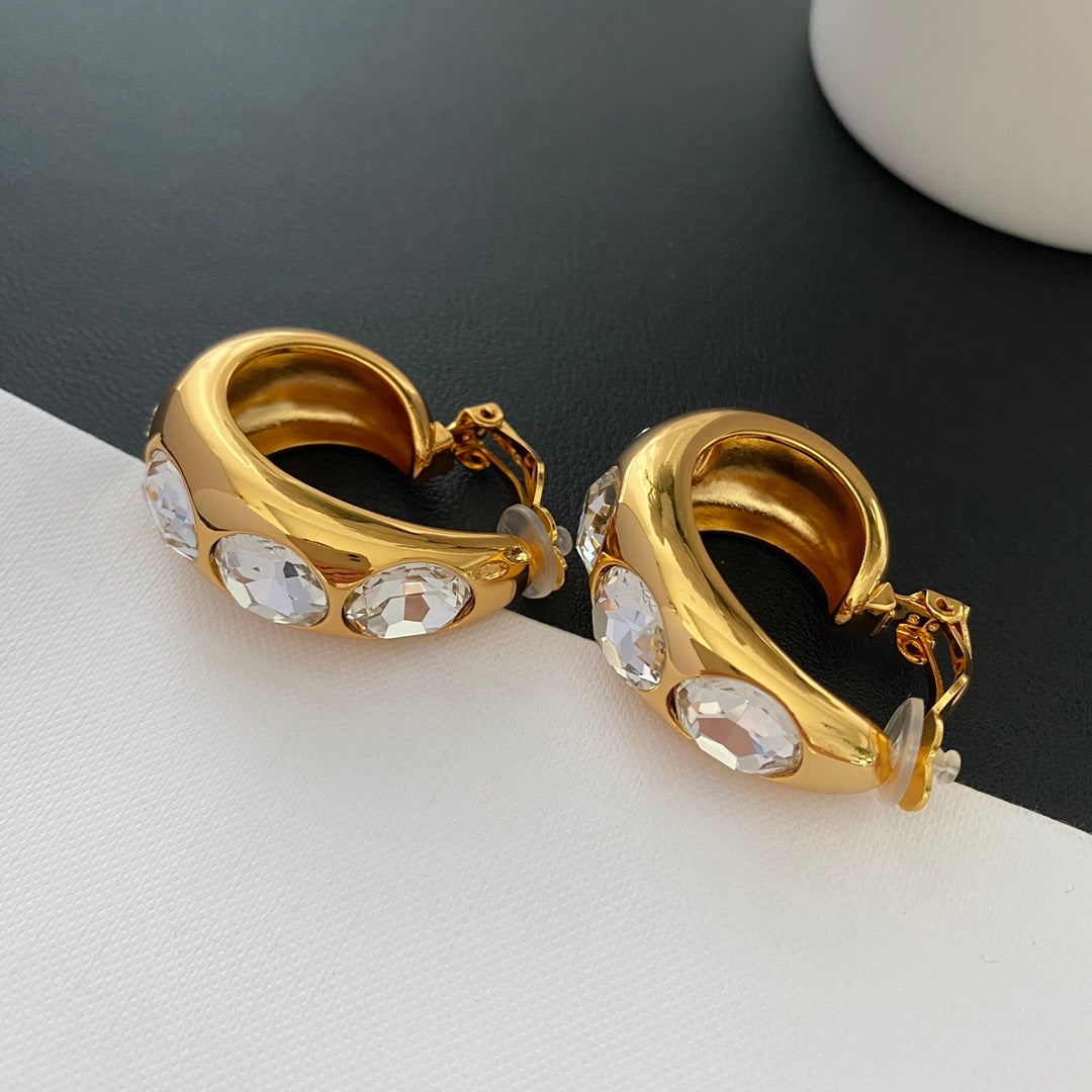 Side view of gold-tone wide hoop clip-on earrings showing hinged clip closures and clear round pads