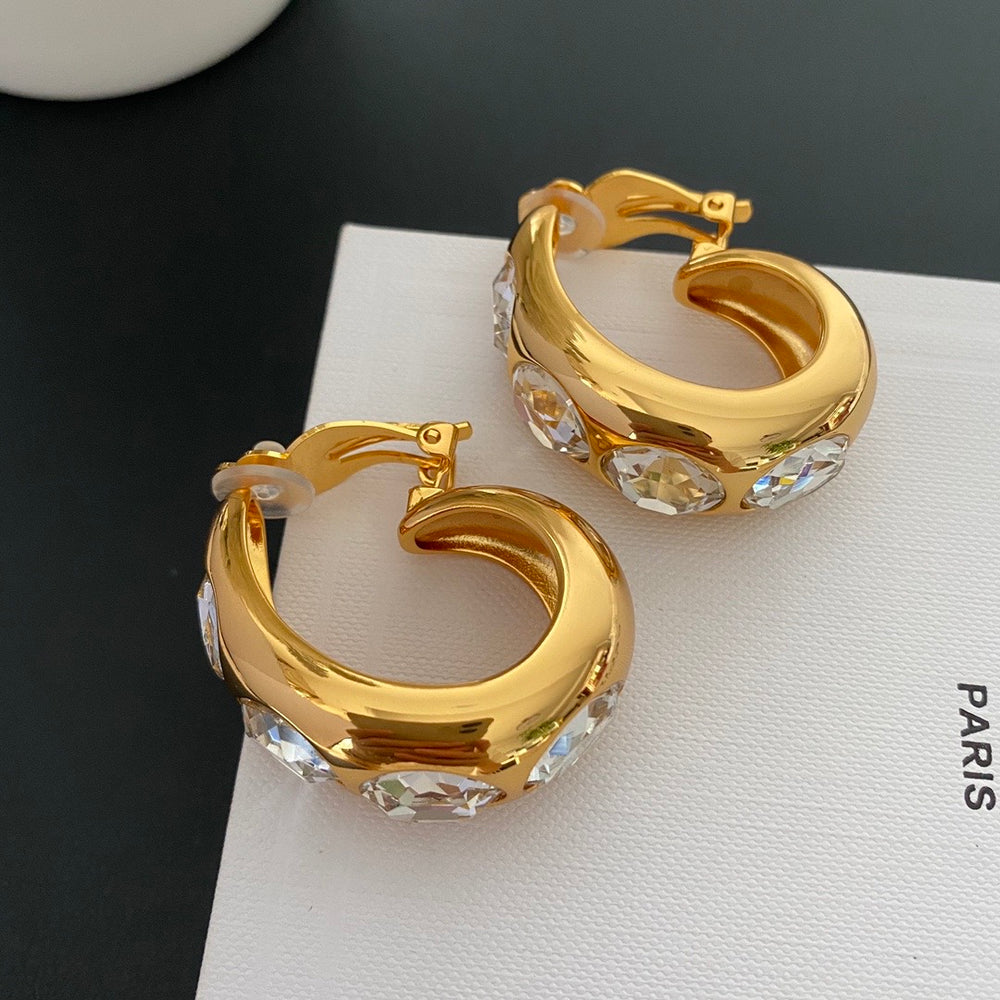 Gold-tone wide hoop clip-on earrings with clear faceted oval crystal-style accents, shown from a front angle