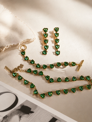 Gold-tone green crystal-style heart necklace, bracelet, and earrings jewelry set flat lay