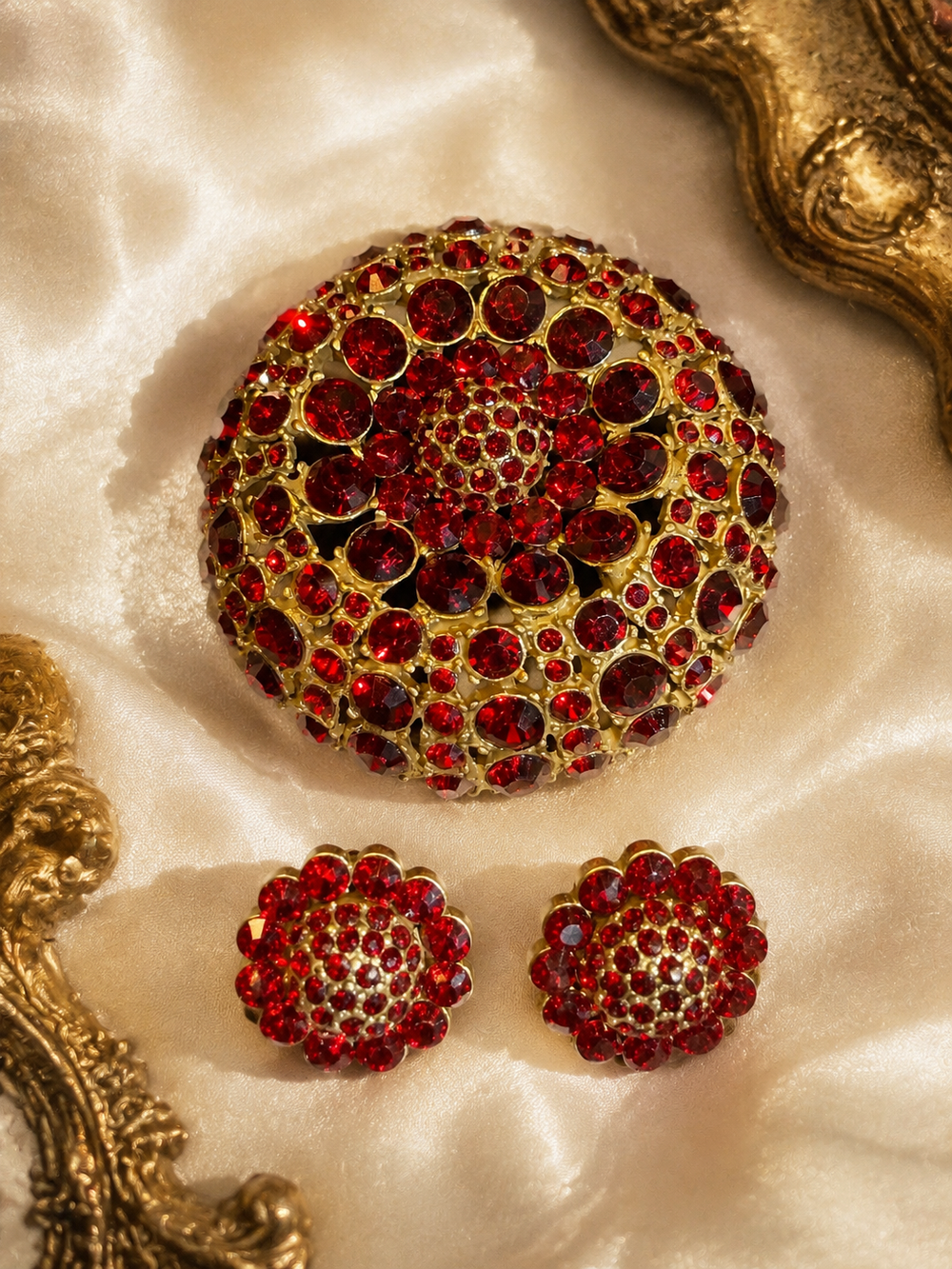 Gold-tone red crystal-style brooch and stud earrings set on light satin background