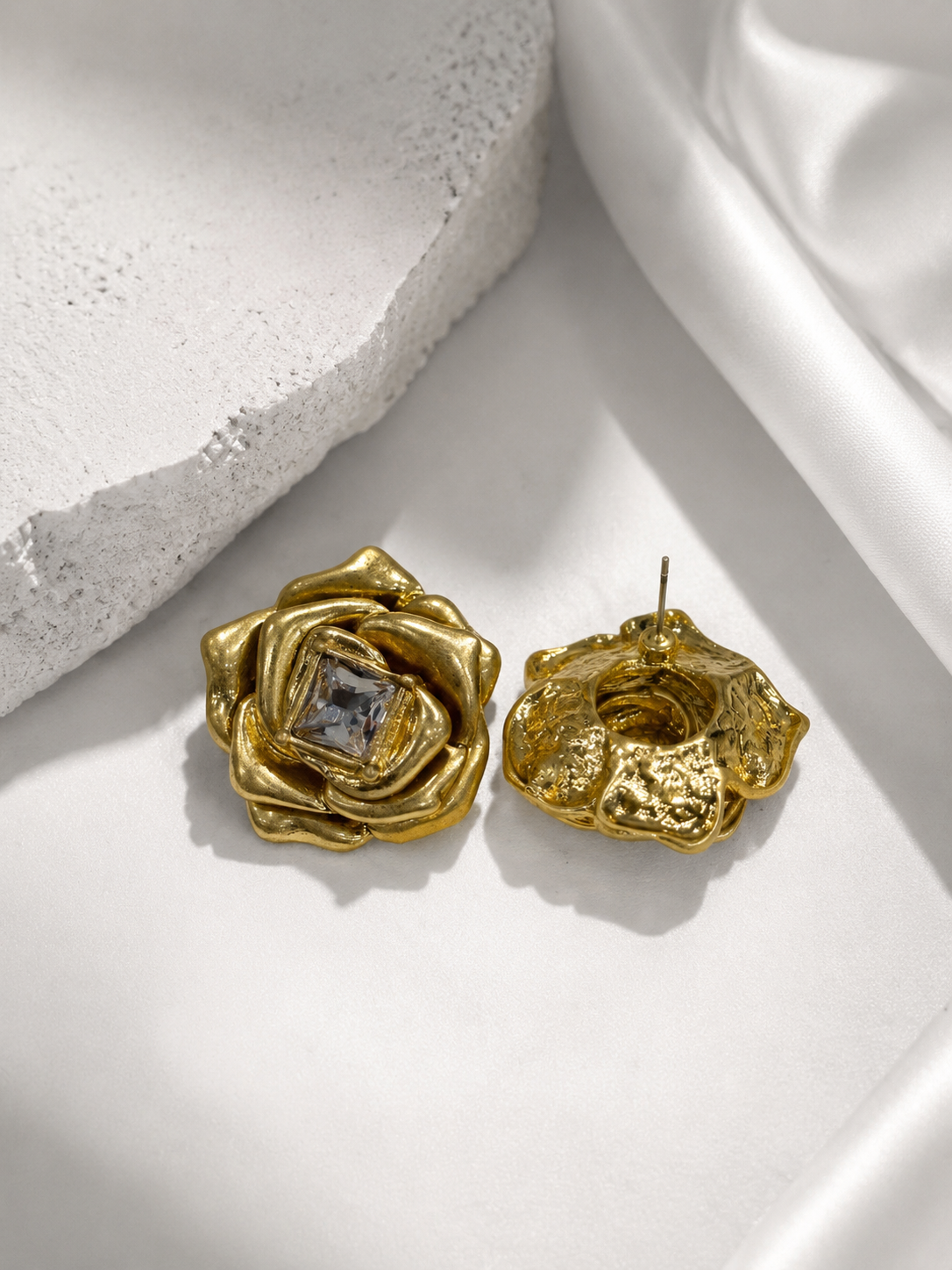 Gold-tone rose-shaped statement stud earrings with clear crystal-style center, detail view
