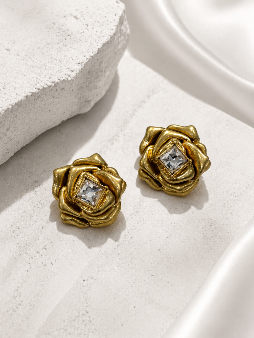 Gold-tone rose-shaped statement stud earrings with clear crystal-style center, front view