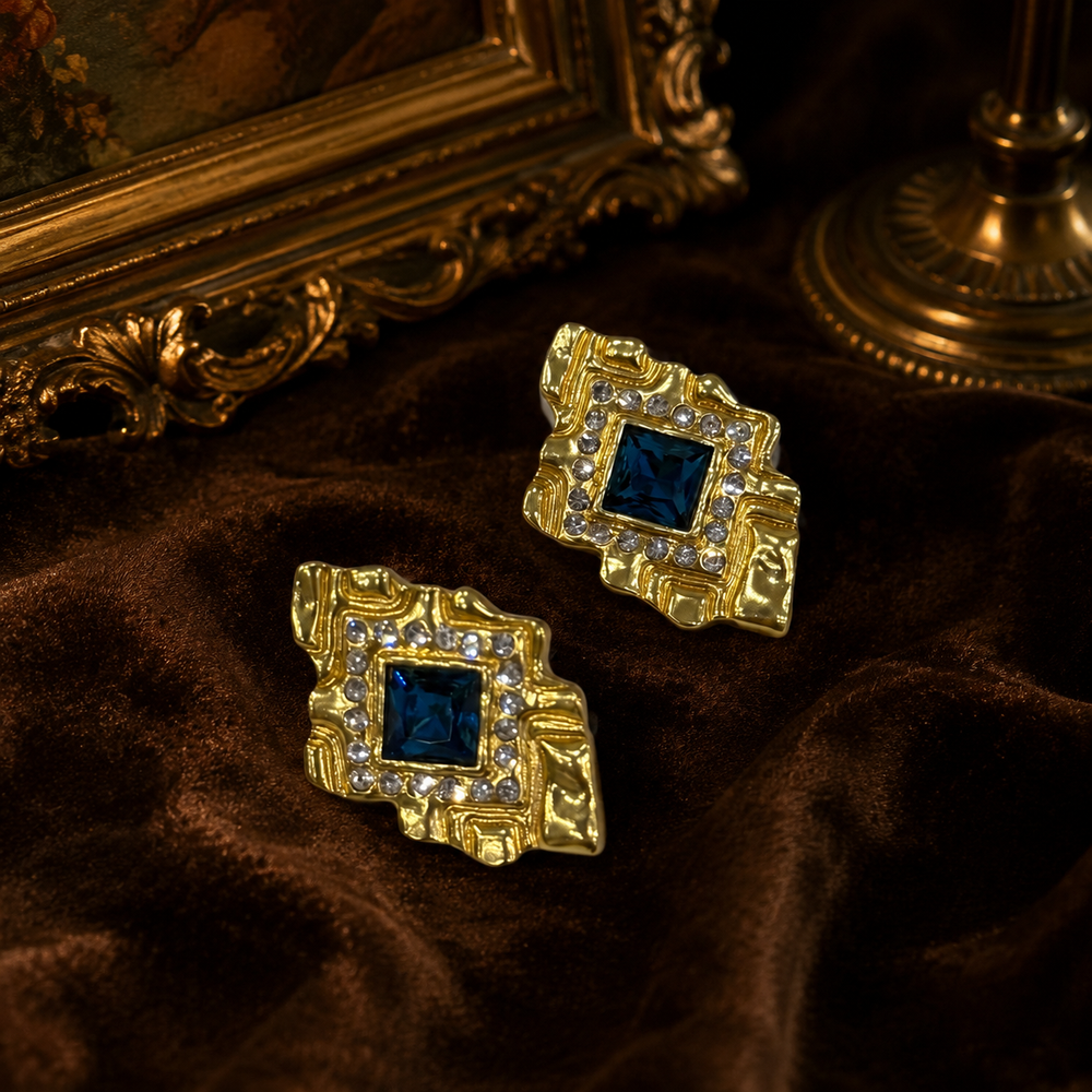 Gold-tone rectangular stud earrings with royal-blue stone-style centers and clear crystal-style accents, front view