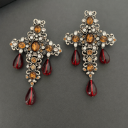 Pair of orange crystal glass cross tassel clip-on earrings on a dark background