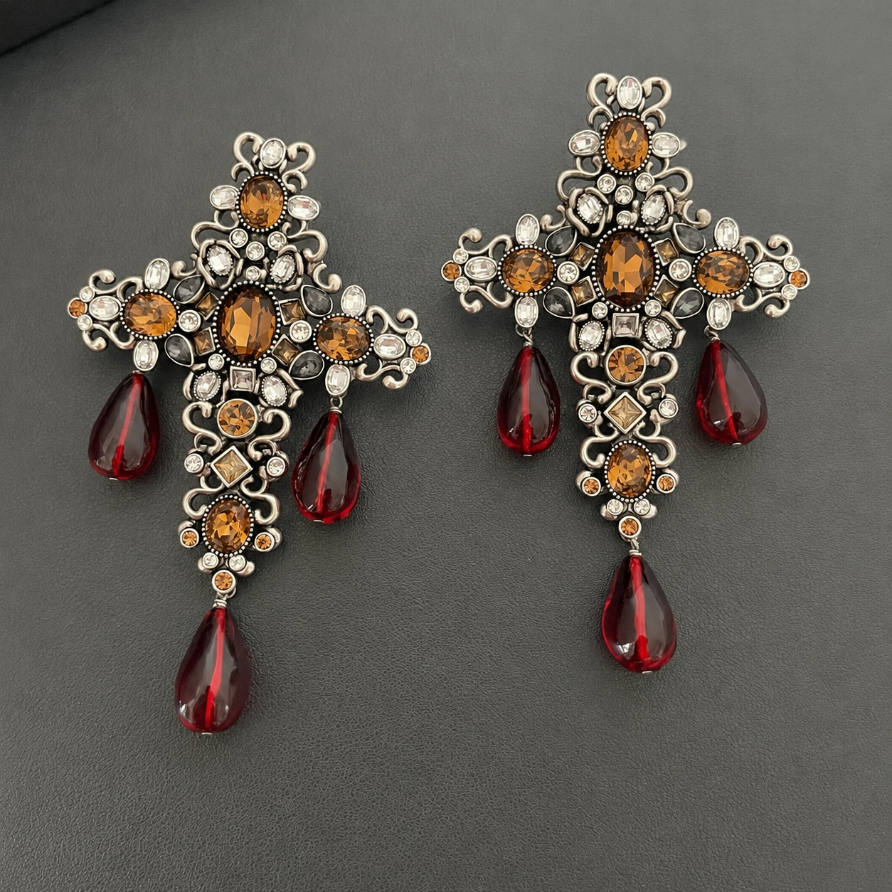 Pair of orange crystal glass cross tassel clip-on earrings on a dark background