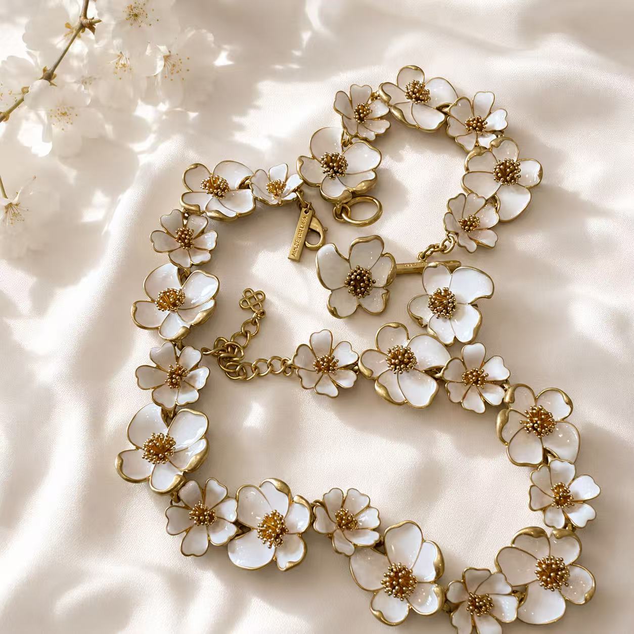 White enamel floral necklace, bracelet, and stud earrings arranged on white satin