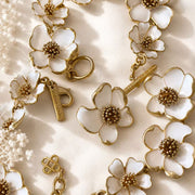 White enamel floral necklace, bracelet, and stud earrings close-up on white satin
